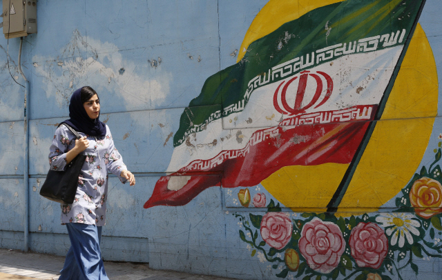 한 여성이 6일(현지시간) 테헤란에서 이란 국기가 그려진 담장 앞을 지나고 있다. /테헤란=AFP연합뉴스