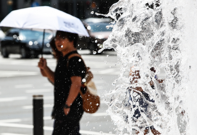 폭염의 기세가 누그러지지 않은 12일 오후 서울시청 앞 분수대 앞을 시민들이 양산을 쓰고 지나치고 있다./연합뉴스