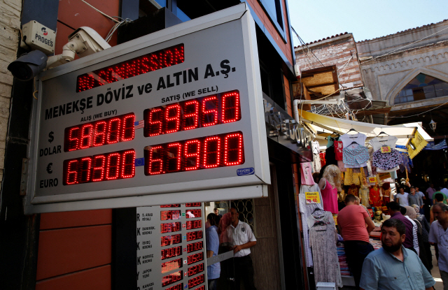 미국이 터키에 가한 제재의 충격으로 터키 리라화 가치가 급락한 10일(현지시간) 이스탄불에서 사람들이 환전소 밖에 있는 환율 시세표를 확인하고 있다../이스탄불=로이터연합뉴스