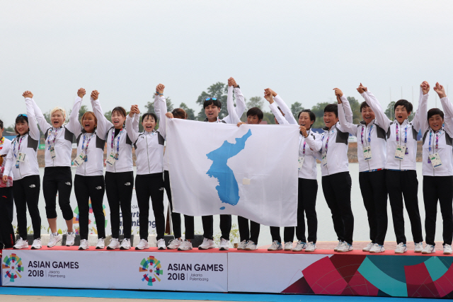 카누 여자 용선 남북 단일팀 선수들이 26일 아시안게임 500m 금메달을 합작한 뒤 손을 잡고 시상대에 올라 한반도기를 펼치며 환호하고 있다. /연합뉴스