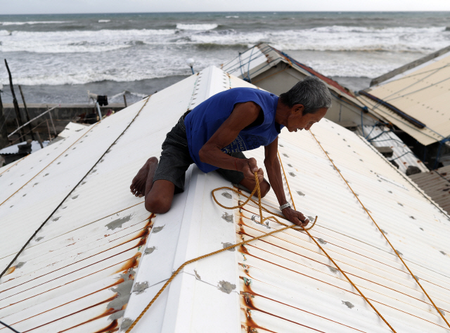 지난 14일 필리핀 마닐라 북부 아파리에서 한 주민이 지붕 위로 올라가 슬레이트를 단단히 묶으며 강풍에 대비하고 있다. 필리핀 적십자사는 태풍 ‘망쿳’의 상륙이 임박한 가운데 약 300만 명이 태풍의 직접적인 이동경로에 거주하고 있으며 700만 명 가량이 영향권에 들어갈 것으로 추산했다. /마닐라=EPA연합뉴스