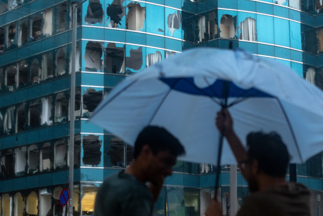 태풍 ‘망쿳’이 강타한 홍콩에서 16일(현지시간) 태풍으로 인해 창문이 깨져 있는 빌딩 앞에서 사람들이 우산을 펼치고 있다./AFP연합뉴스