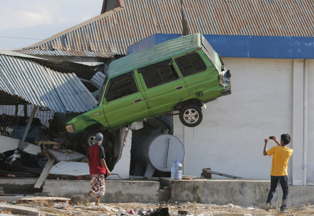 규모 7.5 강진과 쓰나미가 강타한 인도네시아 술라웨시섬 팔루 지역의 탈리세 해변 마을에서 1일(현지시간) 한 주민이 공중으로 올라가 파손된 주택 담벽에 걸려있는 자동차를 모바일폰으로 찍고 있다. /연합뉴스