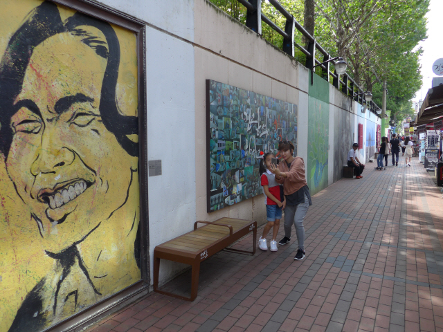 ‘김광석 다시 그리기 길’을 찾은 방문객들이 벽화가 그려진 담벼락을 배경으로 사진을 찍고 있다.