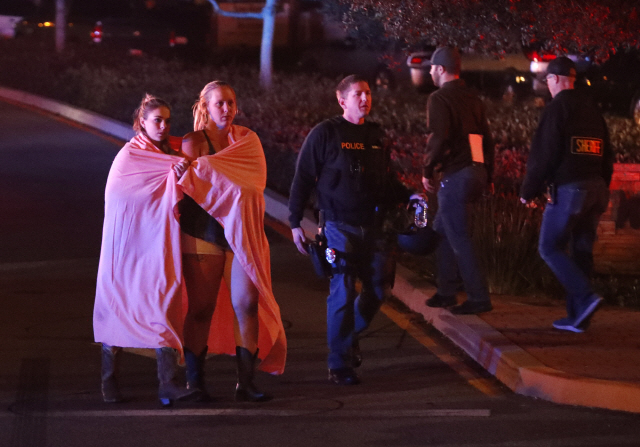 7일(현지시간) 미국 로스앤젤레스 외곽 사우전드오크스에 있는 ‘보더라인 바 & 그릴’에서 발생한 총격사건 현장 주변에 두  여성이 담요를 두르고 사고 현장을 벗어나고 있다. /로스앤젤레스=EPA연합뉴스