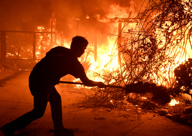 9일(현지시간) 미국 캘리포니아주 말리부에서 한 남성이 주택에 붙은 불을 끄기 위해 안간힘을 쓰고 있다. /말리부=로이터연합뉴스