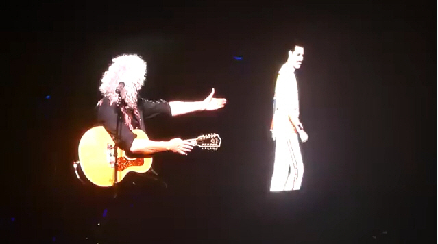 록그룹 ‘퀸’의 기타리스트 브라이언 메이가 공연 중 프레디 머큐리의 영상에 경의를 표하는 손짓을 하고 있다./유튜브캡처