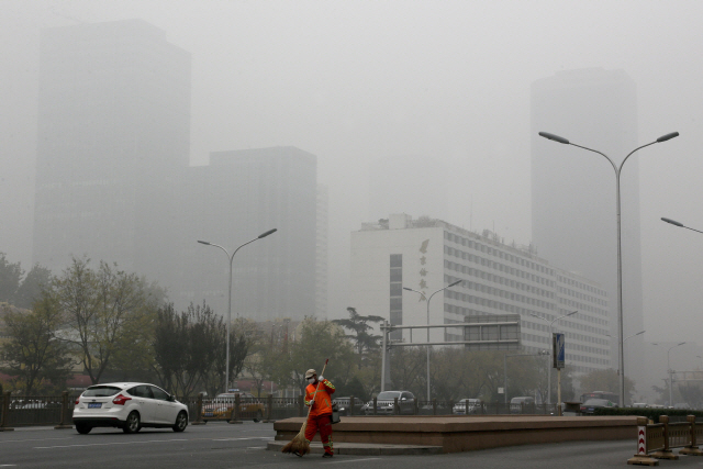 14일 중국 베이징의 고층 건물들이 짙은 스모그에 가려 보이지 않는 가운데 마스크를 쓴 환경미화원이 도로를 청소하고 있다. 이날 베이징의 공기질 지수는 한때 300을 넘어 가장 나쁜 등급인 6급을 나타냈다. 전날에 이어 중국 25개 도시에는 대기오염 황색 경보(세 번째로 높은 단계)가 발령됐으며 짙은 안개가 겹친 일부 지역에서는 차량 통행이 제한되기도 했다. /베이징=AP연합뉴스
