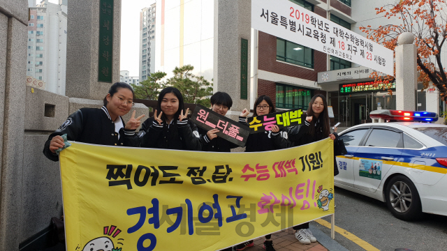 15일 서울 강남구 진선여고 앞에서 경기여고 재학생들이 수험생을 응원하며 포즈를 취하고 있다. 학생들 뒤로 수학능력시험에 늦은 수험생을 태우고 고사장으로 진입하는 경찰차가 보인다./오지현기자