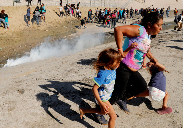 미국 캘리포니아주 샌디에이고와 접경 지역인 멕시코 티후아나에서 25일(현지시간) 미국 국경 진입을 시도하던 온두라스 출신 이주민 모녀가 국경수비대가 발사한 최루탄을 피해 달리고 있다. /티후아나=로이터연합뉴스