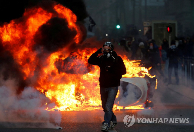 8일(현지시간) 프랑스 남부 마르세유에서 ‘노란조끼’ 시위가 벌어진 가운데 한 시위 참가자 뒤로 자동차가 불에 타고 있다./사진=연합뉴스