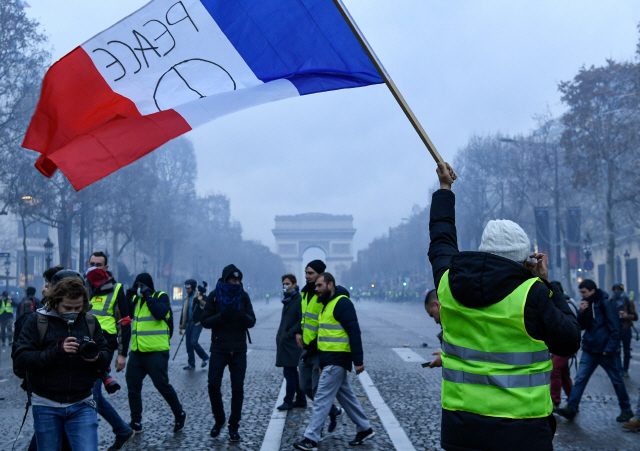 8일(현지시간) 프랑스 수도인 파리 샹젤리제 거리에서 ‘노란 조끼’ 시위대 중 한 명이 ‘평화’라고 적힌 프랑스 국기를 흔들고 있다.  /파리=AFP연합뉴스