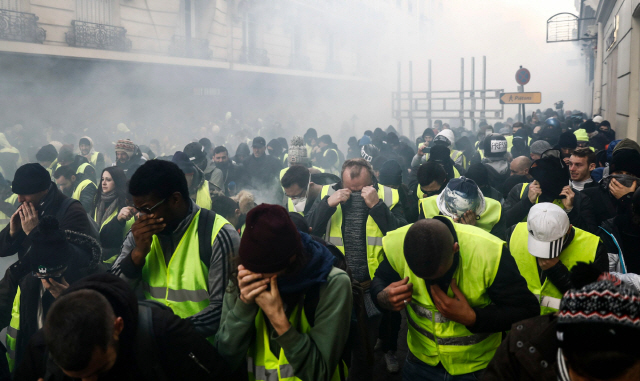 8일(현지시간) 프랑스 수도인 파리 샹젤리제 거리 부근에서 ‘노란 조끼’ 시위대가 경찰이 쏜 최루탄을 피해 얼굴을 가리고 있다. /파리=AFP연합뉴스