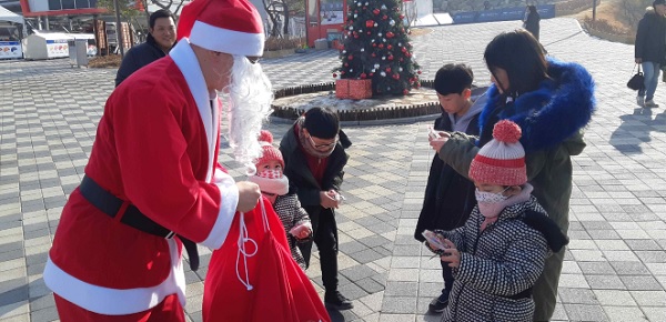 ▲루지를 타고 내려온 산타가 어린이에게 선물을 주고 있다.