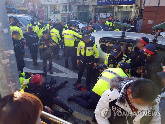 24일 오후 3시 46분께 부산 사상구 덕포동 사상초등학교 인근에서 덕포1구역 재개발 반대 도로 행진 중 돌진한 집회 주최 측 차량에 다친 집회 참가자들이 도로에 앉아 있다. 이 사고로 경찰관과 집회 참가자 20여명이 다쳤다./연합뉴스