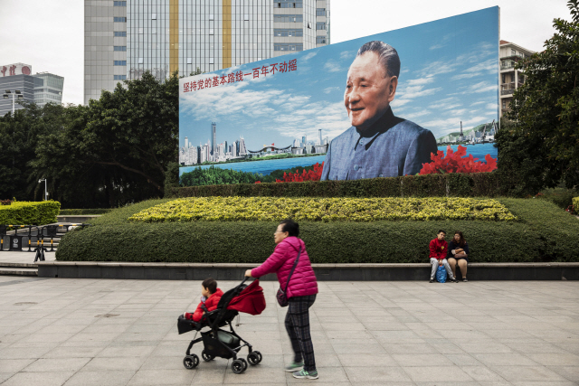 광둥성 선전에서 한 할머니가 아이를 태운 유모차를 끌고 있다. 뒤로는 경제성장을 이유로 ‘1가구 1자녀’ 정책을 도입했던 덩샤오핑의 대형 포스터가 보인다. /블룸버그통신