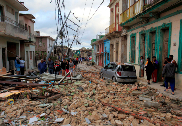 폭우를 동반한 시속 100㎞의 토네이도가 강타한 쿠바 수도 아바나에서 28일(현지시간) 주민들이 전신주가 파손되고 붕괴된 건물 잔해가 나뒹구는 거리를 망연자실한 표정으로 바라보고 있다. /아바나=로이터연합뉴스