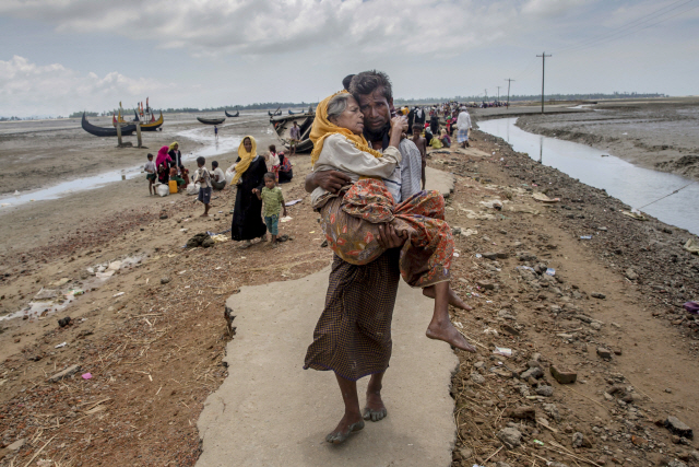 미얀마 정부군의 탄압을 피해 국경을 넘어 방글라데시로 탈출한 이슬람계 소수민족 로힝야족의 한 남성이 자신의 모친을 품에 안은 채 테크나프에 있는 난민 캠프를 향해 걸어가고 있다. / (AP)연합뉴스