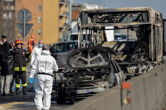 20일(현지시간) 이탈리아 과학수사대와 소방관들이 밀라노 외곽의 도로에서 세네갈 출신의 운전자가 불을 질러 새까맣게 탄 스쿨버스의 잔해를 살피며 현장감식을 벌이고 있다.  /밀라노=AFP연합뉴스