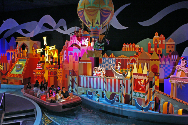 디즈니랜드를 찾은 여행객들이 작은 보트를 타고 세계 각국의 전통 의상을 입은 미니 모형을 구경하고 있다.