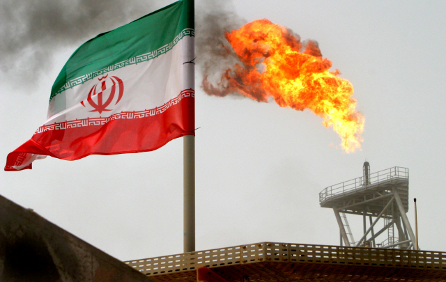 이란 국기 옆 원유 생산시설에서 화염이 치솟고 있다. /로이터연합뉴스
