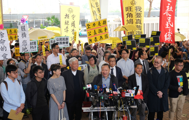 2014년 홍콩에서 열린 대규모 민주화 시위 ‘우산 혁명’을 이끈 9명에 대한 법원의 판결을 앞두고 9일 홍콩 웨스트카우룽 법원 앞에 찬킨만(앞줄 오른쪽 네번째) 홍콩중문대 교수 등 관련 인물 9명이 노란 우산을 든 지지자들 앞에서 기자회견을 하고 있다. /홍콩=로이터연합뉴스