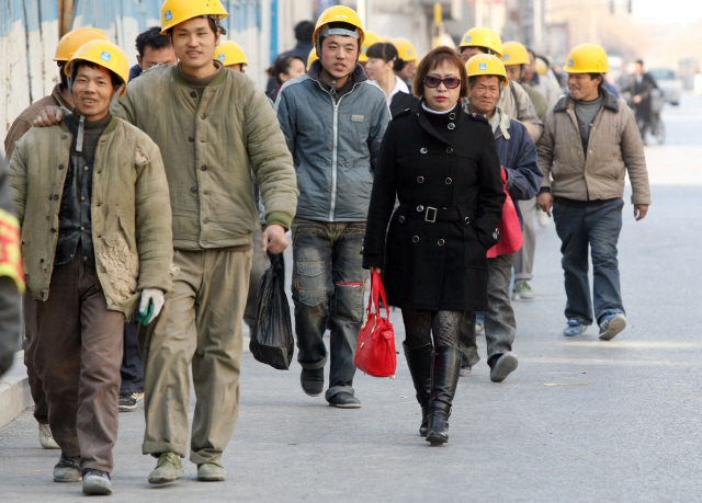 중국 베이징의 한 공사장에서 농민공들이 작업을 위해 이동하고 있다. 농민공들의 밝은 얼굴과 달리 ‘베이징시민’으로 보이는 한 여성의 표정은 굳어 있어 대조적이다. /블룸버그
