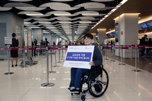 ‘수동휠체어 전동화키트 셰어링’ 서비스를 이용하는 정지영씨가 19일 김포공항 서비스 거점 첫 번째 이용자임을 알리는 알림판을 들고 있다. /사진제공=현대차그룹