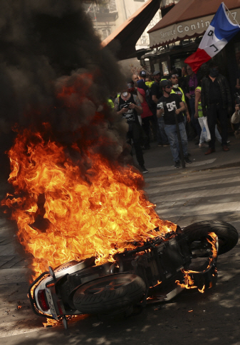 지난 20일(현지시간) 프랑스 파리에서 노란 조끼 시위대가 집회 도중 지른 불로 오토바이가 화염에 휩싸인 가운데 시위대가 프랑스 국기를 흔들며 행진하고 있다.   /파리=AP연합뉴스