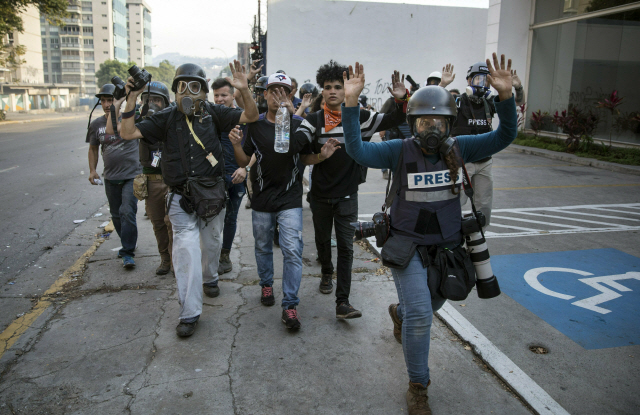 1일(현지시간) ‘한 나라 두 대통령’이라는 초유의 사태를 겪고 있는 베네수엘라에서 임시 대통령을 자처하는 후안 과이도 국회의장을 지지하는 반(反) 정부 시위대와 니콜라스 마두로 현 대통령을 지지하는 친정부 시위대가 충돌한 가운데 현장을 취재 중이던 기자들이 시위대와 구분짓기 위해 두 손을 들고 수도 카라카스 외곽 라 카를로타 공군기지 인근을 지나고 있다. /카라카스=AP연합뉴스