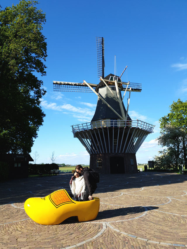 쾨켄호프 정원에 설치된 전통 풍차를 배경으로 관광객들이 노란색 큰 구두에 들어가 보고 있다.