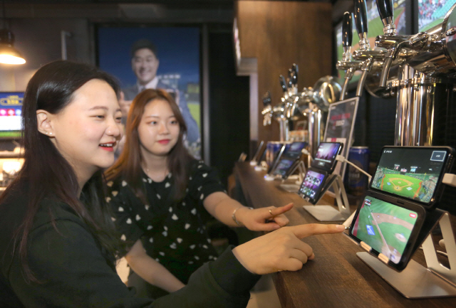 LG유플러스가 서울 강남에 마련한 ‘일상로 5G길’을 찾은 사람들이 ‘V50 씽큐’ 듀얼스크린을 이용해 U+프로야구 중계를 보고 있다. LG유플러스는 5G 서비스를 체험한 사람 10명 중 9명이 만족감을 나타냈다고 밝혔다./사진제공=LG유플러스