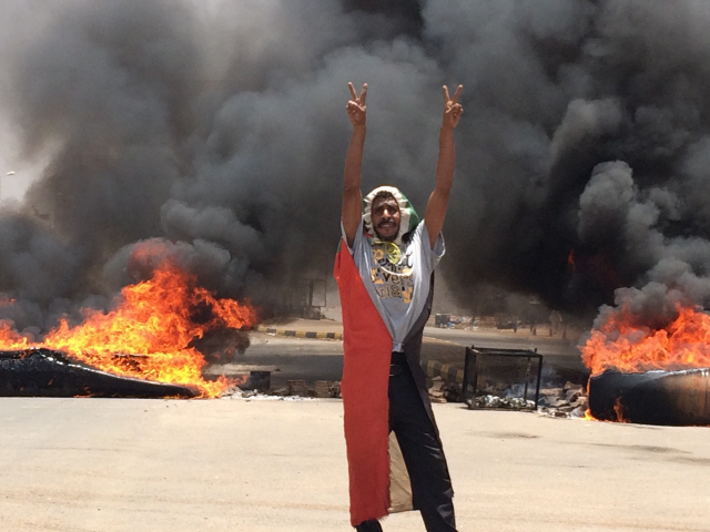 수단의 수도 하르툼의 군 본부 주변 도로에서 3일(현지시간) 불타는 타이어들을 배경으로 한 시위자가 손가락으로 승리를 뜻하는 브이(V)자를 그려 보이고 있다. /하르툼=AP연합뉴스