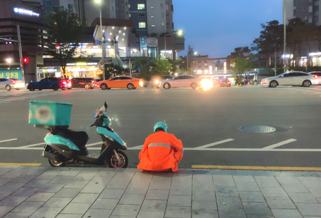 비 예보가 있었던 지난 주말 서울 합정역 인근. 후텁지근한 날씨에 비옷까지 걸쳐입은 배달 라이더가 보도에 앉아 잠시 쉬고 있다. / 강신우 기자