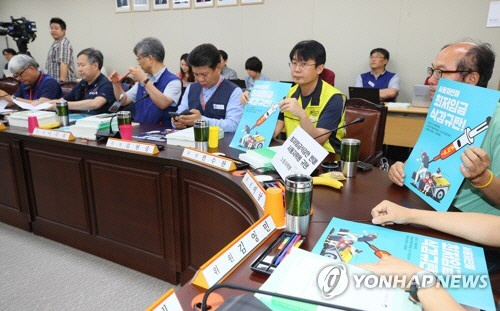 제11차 전원회의에서 근로자 위원들이 사용자 삭감안 규탄 포스터를 들어 보이고 있다./연합뉴스
