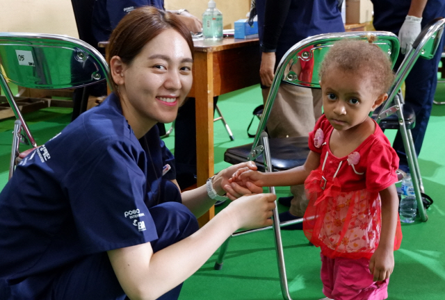 인도네시아 의료 봉사 활동에 참여한 포스코인터내셔널 직원이 파푸아주 어린이의 손을 잡은 채 활짝 웃고 있다./사진제공=포스코인터내셔널