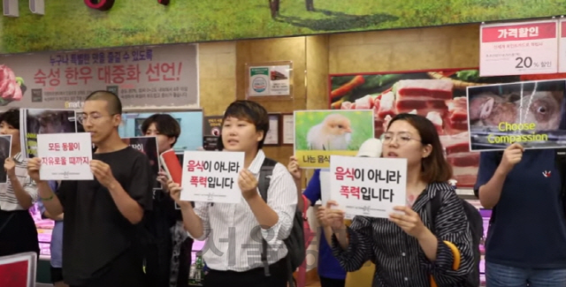 디렉트액션에브리웨어(Direct Action Everywhere·DxE, 이하 디엑스이) 서울은 지난 15일 유튜브 계정을 통해 이마트의 모 지점 정육 코너에서 ‘방해시위’를 벌인 영상을 공개했다. 영상 속 활동가들은 마트 정육 판매대에 진열된 고기에 국화꽃을 놓는 퍼포먼스를 진행했으며 ‘음식이 아니라 폭력입니다’, ‘모든 동물이 자유로울 때까지’ 등 피켓을 들고 시위를 벌였다./디엑스이 서울 유튜브 계정 영상 캡처