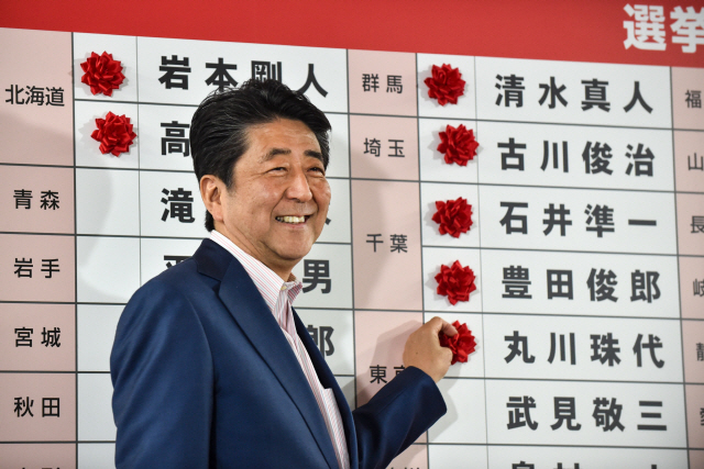 아베 신조 일본 총리가 21일 참의원선거 종료 후 도쿄 자민당 당사에서 당선자들의 이름에 꽃을 달며 환하게 웃고 있다. /도쿄=AFP연합뉴스