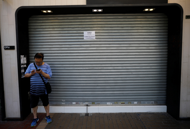 ‘범죄인 인도 법안’(송환법) 반대로 총파업이 벌어진 5일 홍콩에서 한 남성이 한 상점의 닫힌 셔터 앞에서 휴대전화를 보고 있다. 셔터에는 교통상 지장으로 이날 하루 휴업한다는 게시문이 붙어 있다. /홍콩=로이터연합뉴스