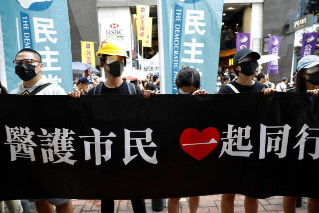 18일(현지시간) 홍콩에서 열린 송환법 반대시위 참가자들이 ‘의료기관 종사자들과 시민들이 함께 행진한다’고 쓰인 현수막을 들고 서 있다.  /홍콩=AP연합뉴스