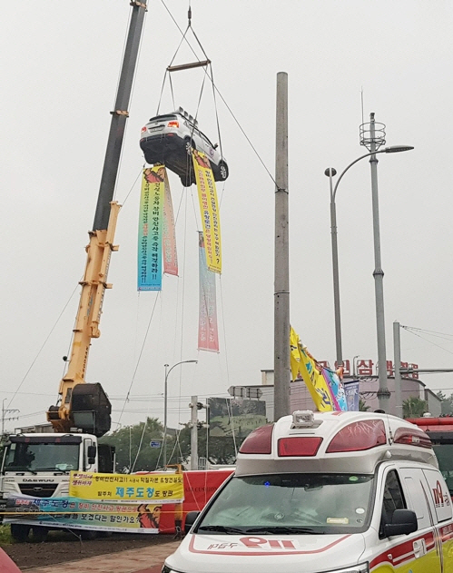 제주지역 건설노동자가 20일 오전 제주시 연동 신광사거리 앞에서 크레인에 스포츠유틸리티(SUV) 차량을 매단 채 약 10ｍ 상공에서 이틀째 고공 시위를 벌이고 있다. /사진제공=제주도소방서