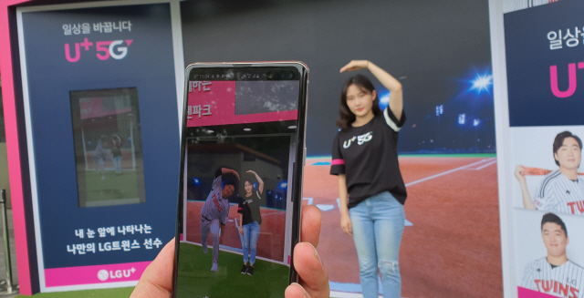 LG유플러스 직원이 5일 서울 잠실야구장 1루측 광장에 마련된 ‘AR 팬파크’에서 5G 스마트폰 안에 등장한 LG트윈스 임찬규 선수와 함께 하트를 그리고 있다./사진제공=LG유플러스