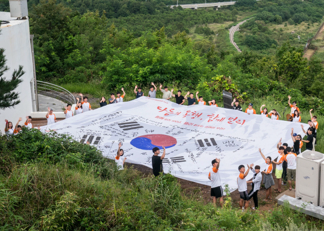 지난 6일 강원도 고성군 통일전망대에서 ‘한화 자전거 평화 여행-다름의 동행, 함께 멀리’ 행사에 참석한 남북 청소년들이 대형 태극기를 펼치고 손을 흔들고 있다./사진제공=한화