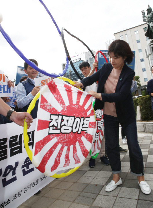 부산겨레하나 회원들이 지난 20일  부산 동구 강제징용노동자상 앞에서 도쿄올림픽 욱일기 사용반대 선언운동 선포 기자회견을 한 후 오륜기 테두리에서 욱일기를 뜯어내는 퍼포먼스를 하고 있다./연합뉴스