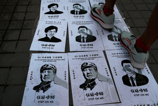 28일(현지시간) 홍콩 도심에서 ‘우산 혁명’ 5주년 기념 집회가 열린 가운데 한 시민이 완차이 지역 길바닥에 붙어 있는 중국의 시진핑 국가주석과 마오쩌둥 전 국가주석, 홍콩의 캐리 람 행정장관의 포스터 사진들을 밟고 지나가고 있다. /홍콩=로이터연합뉴스