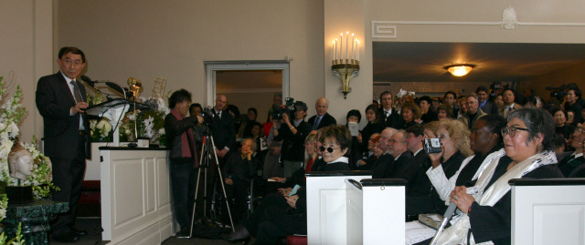 백남준의 장조카인 켄 백 하쿠다(맨 왼쪽)이 2006년 2월 3일 뉴욕에서 열린 장례식에서 추도사를 하던 중 백남준의 유명한 퍼포먼스인 넥타이 자르기를 제안하고 있다. 백남준의 부인이자 미디어아티스트인 구보다 시게코(맨 오른쪽)가 지팡이를 짚고 침통한 표정으로 앉아있다. /사진제공=윤정미