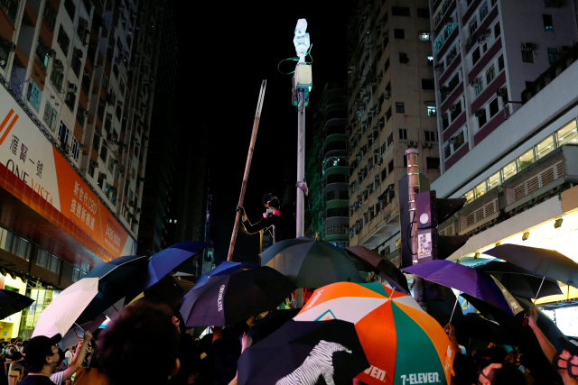 마스크 착용을 금지하는 ‘복면금지법’ 시행을 앞두고 홍콩의 반정부 시위대가 CCTV 카메라를 부수기 위해 가로등을 올라가고 있다. /로이터-연합뉴스
