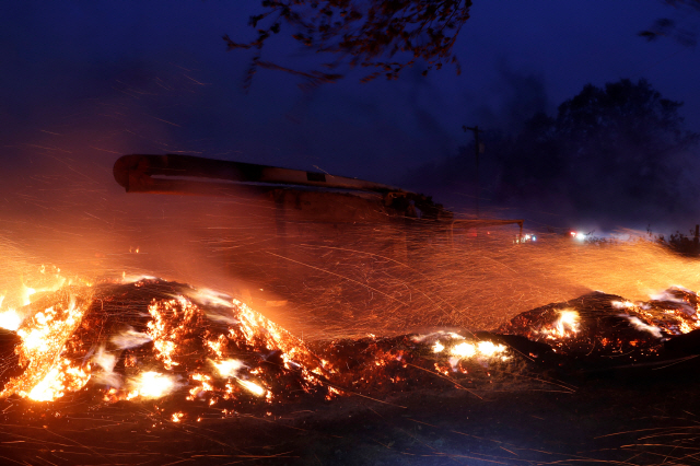 산불이 발생한 미국 캘리포니아주에 27일(현지시간) 강풍이 몰아치면서 소노마 카운티의 힐즈버그에서 트럭이 불타고 불똥이 주위로 날아가고 있다. /힐즈버그=로이터연합뉴스