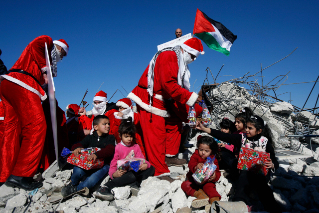 23일(현지시간) 팔레스타인 베들레헴 근교에서 산타복장을 한 팔레스타인인들이 이스라엘의 공격으로 파괴된 집 잔해 위에 앉아 있는 아이들에게 선물을 나눠주고 있다.    /베들레헴=AFP연합뉴스