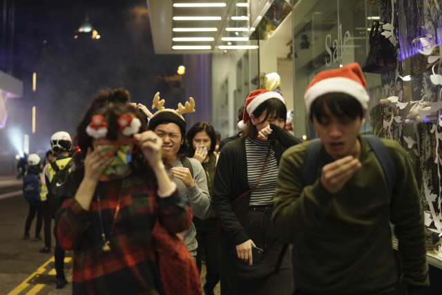 크리스마스 이브인 지난 24일(현지시간) 밤 홍콩에서 산타클로스 모자와 순록 뿔 모양의 머리띠를 착용한 반정부 시위대가 경찰이 쏜 최루가스를 피해 달아나고 있다./홍콩=AP연합뉴스
